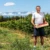 Agriculteur souriant dans un verger, tenant une cagette de nectarines sous un ciel bleu, avec le Canigou en arrière-plan.